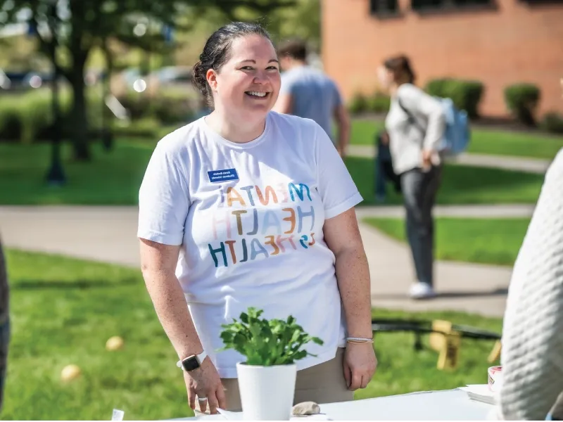 Woman at booth wearing mental health advocacy shirt.